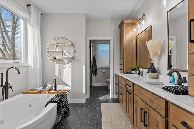 bathroom featuring toilet, plenty of natural light, a tub with jets, and a sink