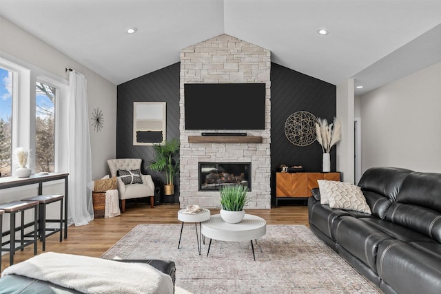 living area with an accent wall, wood finished floors, vaulted ceiling, a stone fireplace, and recessed lighting