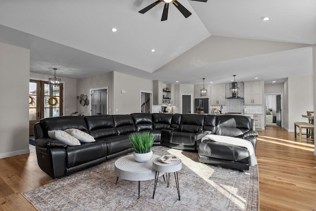 living area with lofted ceiling, ceiling fan with notable chandelier, light wood-type flooring, and baseboards