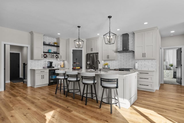 kitchen featuring stainless steel fridge, wall chimney exhaust hood, a breakfast bar, light countertops, and open shelves