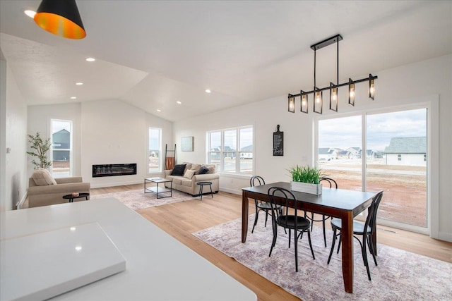 dining space featuring light wood-type flooring, a glass covered fireplace, lofted ceiling, and recessed lighting