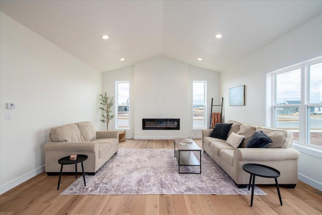 living area with lofted ceiling, light wood finished floors, plenty of natural light, and a glass covered fireplace