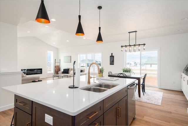 kitchen featuring stainless steel dishwasher, vaulted ceiling, a sink, and light wood finished floors