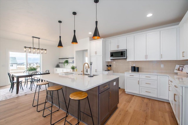 kitchen with tasteful backsplash, stainless steel microwave, a sink, and light wood finished floors