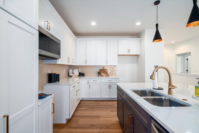 kitchen with light countertops, stainless steel microwave, a sink, and white cabinets