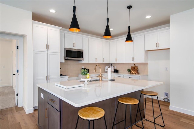 kitchen with a sink, white cabinetry, light countertops, light wood-type flooring, and stainless steel microwave