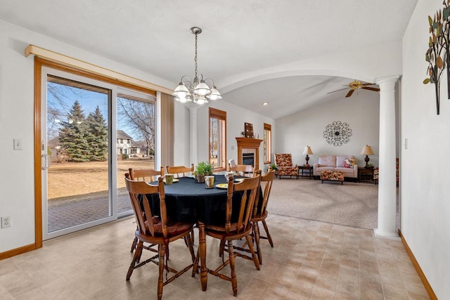 dining room with baseboards, lofted ceiling, decorative columns, arched walkways, and a glass covered fireplace