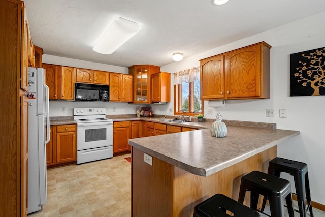 kitchen featuring white appliances, a breakfast bar area, a peninsula, a sink, and brown cabinets