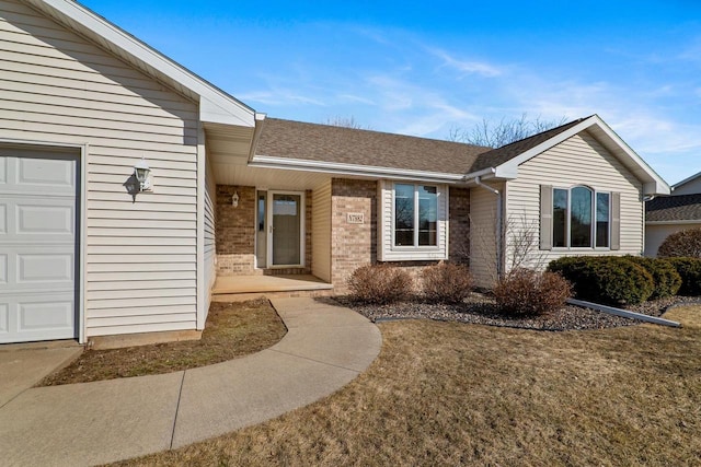 view of exterior entry featuring brick siding, roof with shingles, and an attached garage