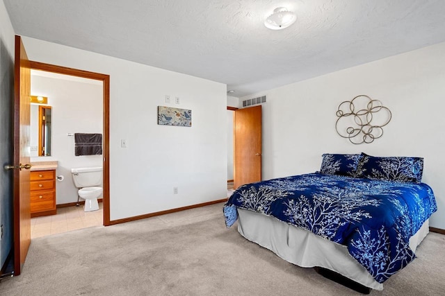 bedroom featuring baseboards, visible vents, ensuite bath, a textured ceiling, and light carpet