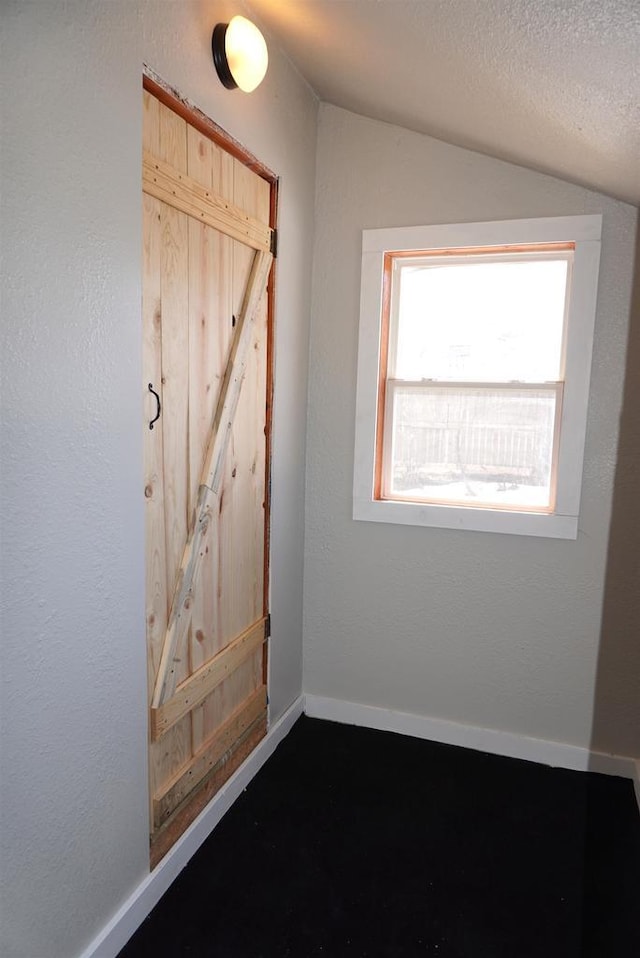 interior space with baseboards, vaulted ceiling, a textured ceiling, and a textured wall