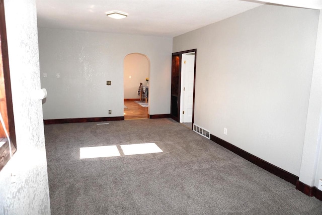 carpeted spare room featuring arched walkways, visible vents, and baseboards