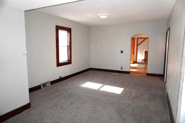 spare room featuring arched walkways, carpet, visible vents, and baseboards