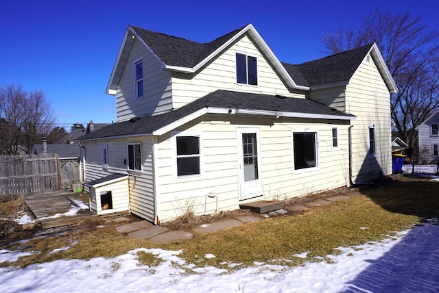 snow covered back of property featuring roof with shingles and fence