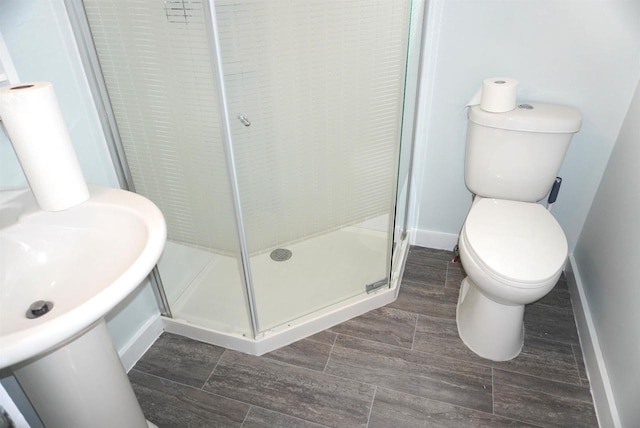 bathroom featuring a stall shower, baseboards, toilet, wood finish floors, and a sink