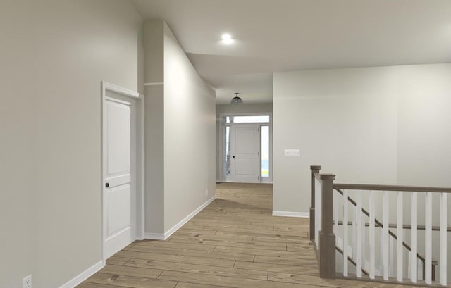 hallway featuring light wood-style floors, baseboards, and an upstairs landing