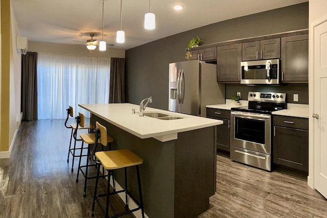 kitchen with an island with sink, a breakfast bar area, dark wood-style flooring, stainless steel appliances, and a sink