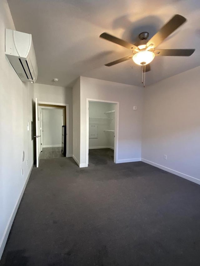 unfurnished bedroom featuring a wall unit AC, baseboards, a spacious closet, and dark carpet