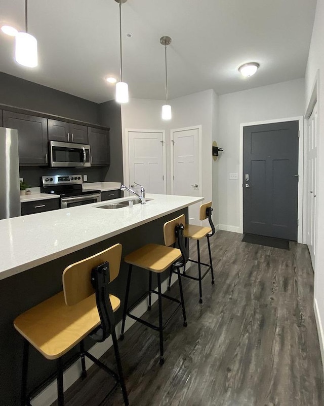 kitchen with a sink, a kitchen breakfast bar, light countertops, appliances with stainless steel finishes, and dark wood finished floors