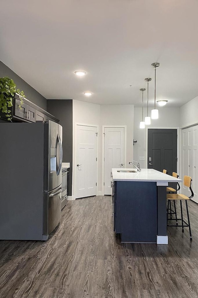 kitchen with stainless steel fridge with ice dispenser, dark wood-style flooring, a kitchen island with sink, light countertops, and a sink