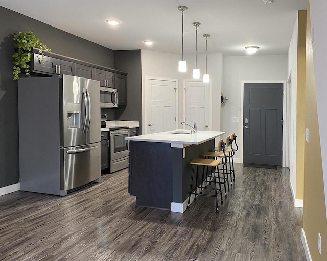 kitchen featuring dark wood-style floors, stainless steel appliances, light countertops, a kitchen bar, and a sink