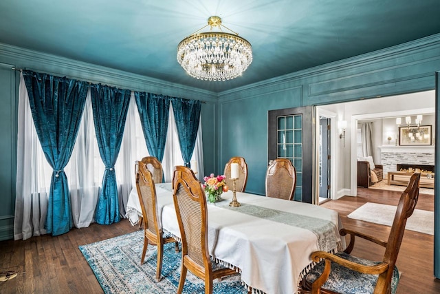 dining area featuring a lit fireplace, ornamental molding, a notable chandelier, and wood finished floors