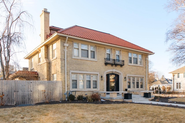 view of front facade featuring brick siding, a chimney, a front yard, and fence