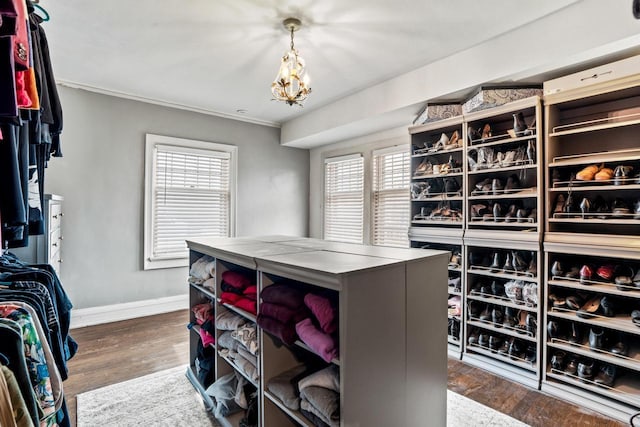 walk in closet with dark wood finished floors and a notable chandelier