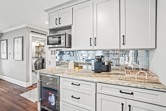 kitchen with beverage cooler, ornamental molding, independent washer and dryer, decorative backsplash, and stainless steel microwave