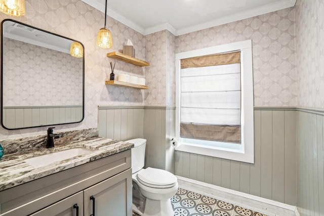 bathroom with toilet, ornamental molding, wainscoting, vanity, and wallpapered walls