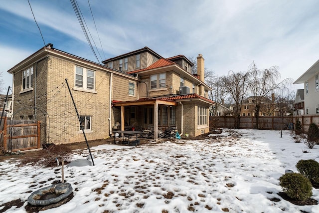 snow covered back of property featuring a chimney, fence, and brick siding