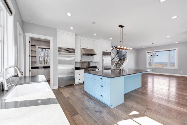 kitchen with built in fridge, dark wood-style flooring, a sink, and under cabinet range hood