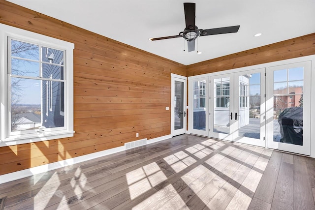 unfurnished room with french doors, wood walls, hardwood / wood-style floors, and a healthy amount of sunlight