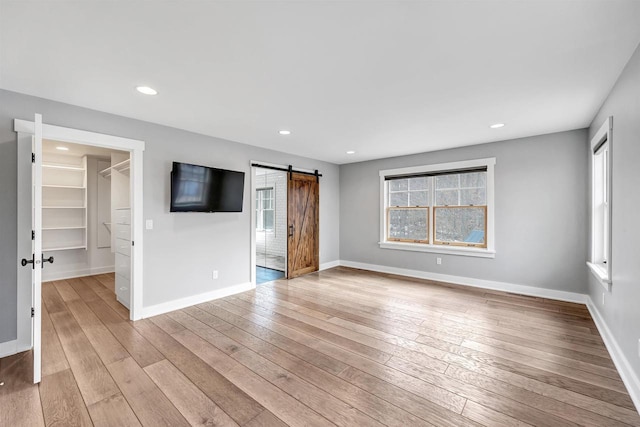 interior space featuring baseboards, multiple windows, light wood finished floors, and a barn door