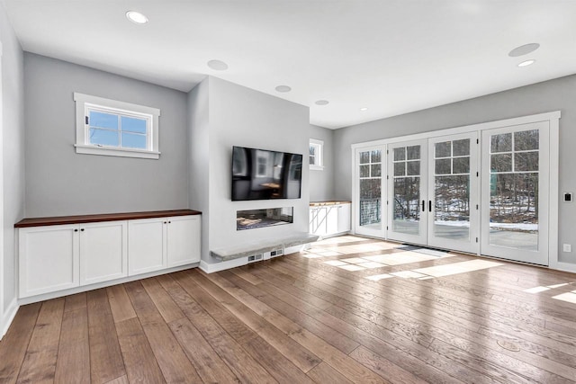 unfurnished living room with french doors, a glass covered fireplace, hardwood / wood-style flooring, and recessed lighting