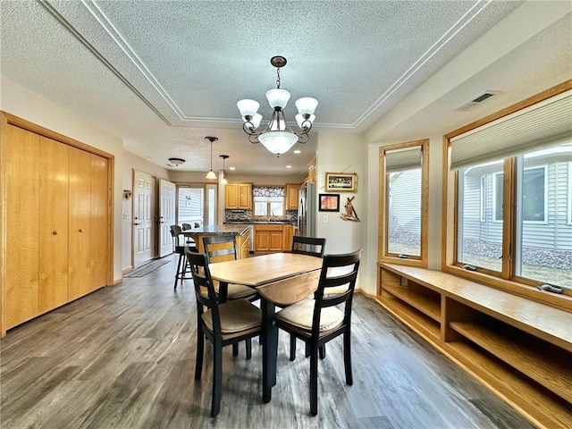 dining area featuring visible vents, dark wood finished floors, a textured ceiling, and an inviting chandelier