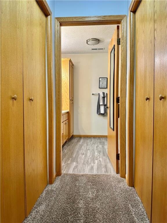 corridor featuring light wood-style floors, visible vents, baseboards, and a textured ceiling