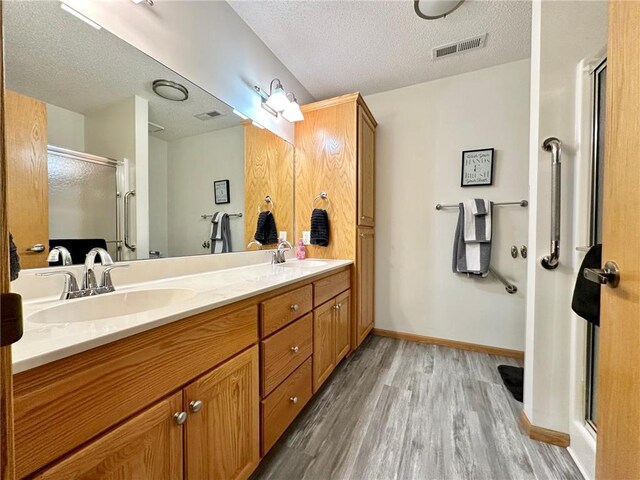 full bath featuring visible vents, a sink, a shower stall, and a textured ceiling