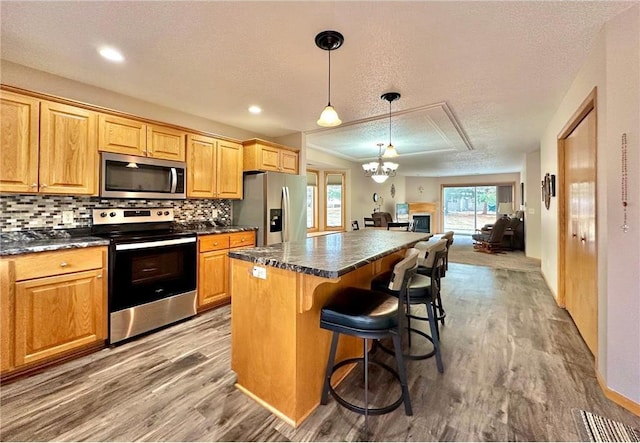 kitchen with a breakfast bar, wood finished floors, a center island, appliances with stainless steel finishes, and decorative backsplash