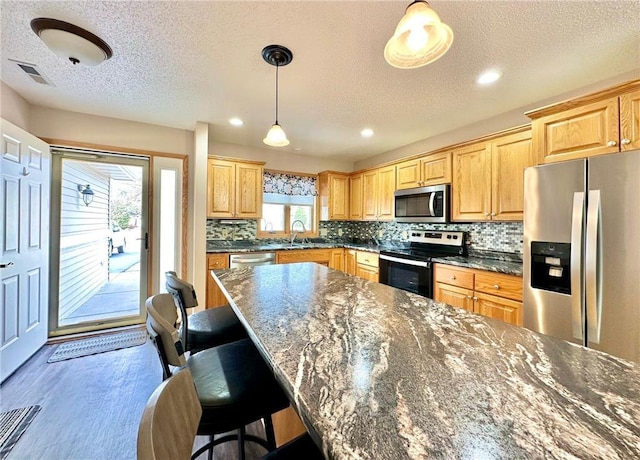 kitchen featuring pendant lighting, stainless steel appliances, tasteful backsplash, a sink, and a kitchen bar