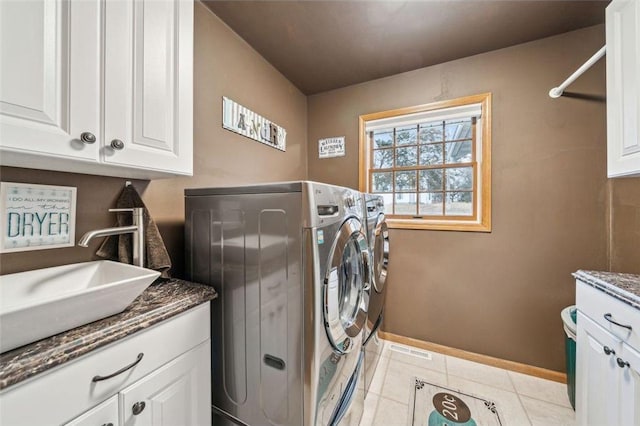 laundry area featuring cabinet space, light tile patterned floors, baseboards, washer and clothes dryer, and a sink