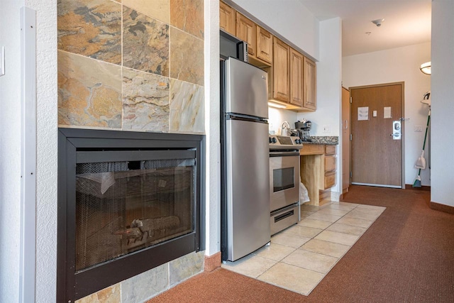 kitchen with light carpet, stainless steel appliances, light tile patterned flooring, and a glass covered fireplace