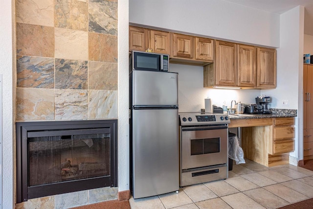 kitchen featuring light tile patterned floors, stainless steel appliances, a sink, a tiled fireplace, and dark countertops