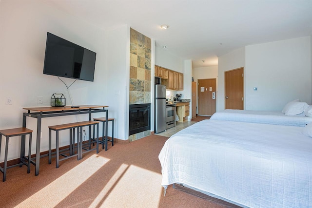 bedroom with light carpet, baseboards, a tiled fireplace, and freestanding refrigerator