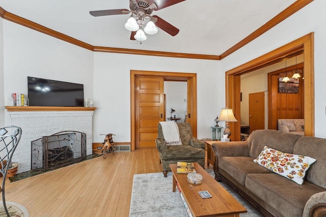 living room with a fireplace, a ceiling fan, crown molding, and wood finished floors