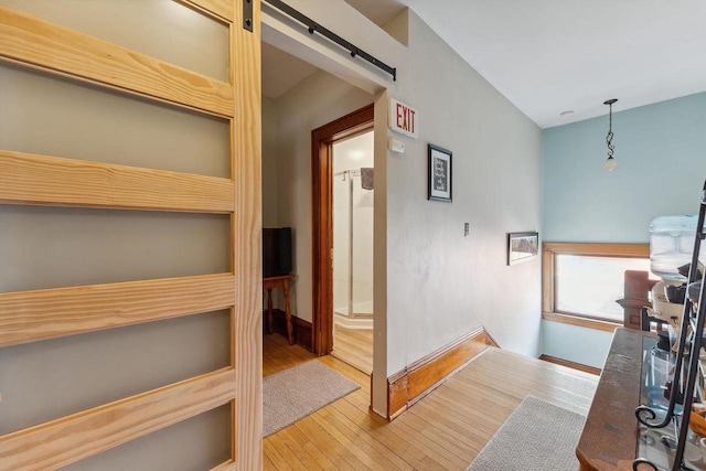 hallway with a barn door, hardwood / wood-style floors, and baseboards