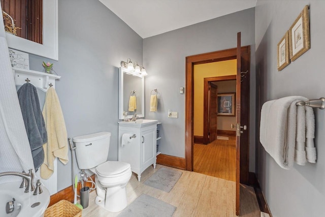 bathroom featuring toilet, a bathing tub, vanity, wood finished floors, and baseboards