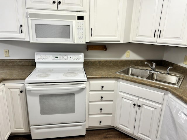 kitchen with white appliances, dark countertops, a sink, and white cabinetry