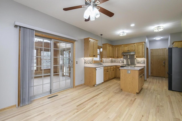 kitchen with light countertops, freestanding refrigerator, a sink, dishwasher, and under cabinet range hood