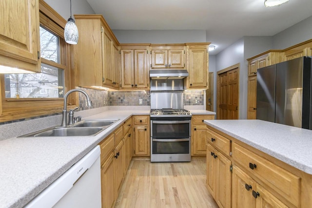 kitchen with appliances with stainless steel finishes, light countertops, a sink, and under cabinet range hood